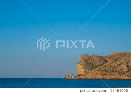 A large rocky promontory rises above the blue sea A large rocky promontory rises above the blue sea 93461096