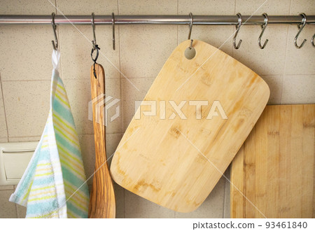 A close-up of cutting wooden boards, a cooking spatula, a kitchen towel hanging on hooks in the kitchen, against the background of a tiled wall 93461840