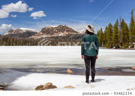 Woman Standing by Snow Covered Lake surrounded by Trees and Mountains. Woman Standing by Snow Covered Lake surrounded by Trees and Mountains. 93462134