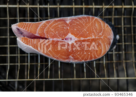 Close up of fresh salmon steak prepared for grilling with grains of salt on it, lies on grill mesh Close up of fresh salmon steak prepared for grilling with grains of salt on it, lies on grill mesh 93465346