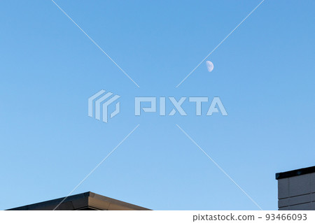 A half moon floating in the blue sky above a residential area 93466093