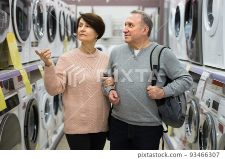 Mature man and woman choosing washing machine in appliance shop 93466307
