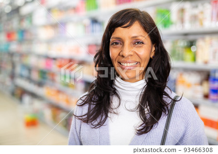 Cheerful Hispanic woman on blurred background of cosmetics store showcase Cheerful Hispanic woman on blurred background of cosmetics store showcase 93466308