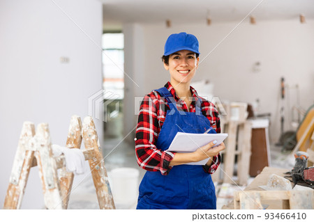 Woman in blue overalls checking completed construction work on drawing 93466410