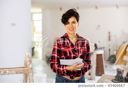 Woman engineer in red shirt and short shorts smiling and checking documents during repair works Woman engineer in red shirt and short shorts smiling and checking documents during repair works 93466667