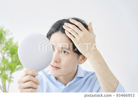 A man holding a hand mirror at home and looking at his hair A man holding a hand mirror at home and looking at his hair 93466953