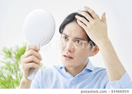 一個男人在家裡拿著一面手鏡，看著自己的頭髮 93466954