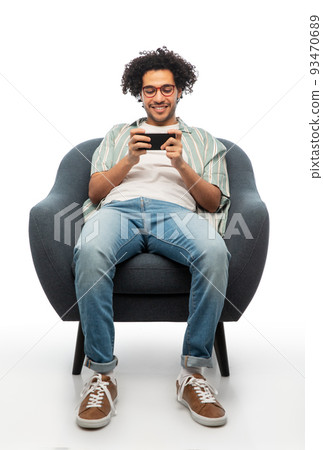 smiling young man with smartphone sitting in chair smiling young man with smartphone sitting in chair 93470689