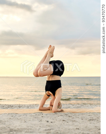 woman doing yoga headstand on beach 93470770