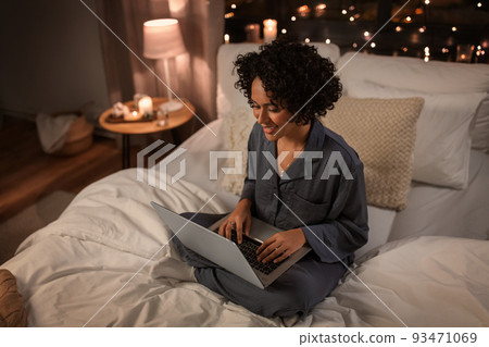 happy woman with laptop sitting in bed at night happy woman with laptop sitting in bed at night 93471069