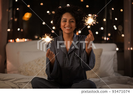 happy woman with sparklers sitting in bed at night happy woman with sparklers sitting in bed at night 93471074