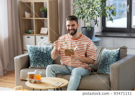 smiling man eating takeaway food at home 93471131