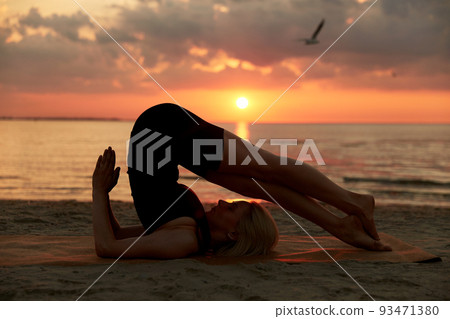woman doing yoga plow pose on beach 93471380