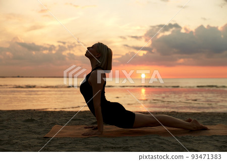 woman doing yoga upward facing dog pose on beach 93471383