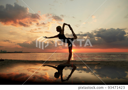 woman doing yoga dancer pose on beach over sunset 93471423