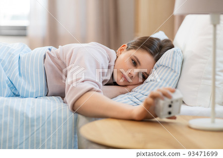 girl looking at alarm clock in bed in morning girl looking at alarm clock in bed in morning 93471699