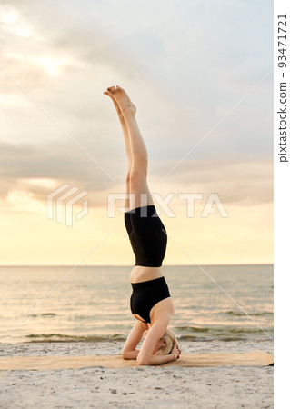 woman doing yoga headstand on beach 93471721