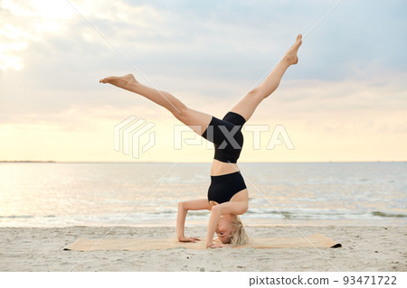 woman doing yoga headstand on beach 93471722