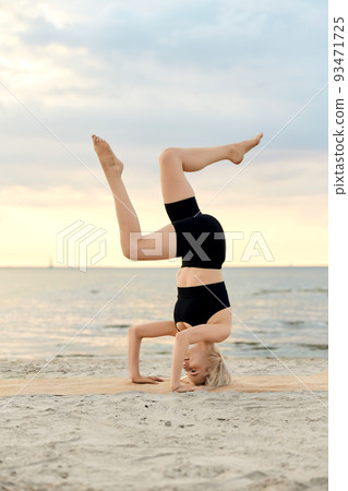 woman doing yoga headstand on beach 93471725