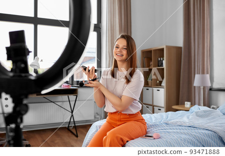 girl blogger with ring light applying make up 93471888