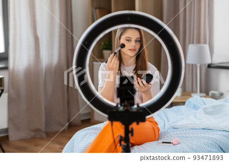 girl blogger with ring light applying make up 93471893
