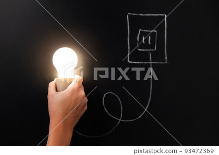 close up of hand holding lightbulb over chalkboard 93472369