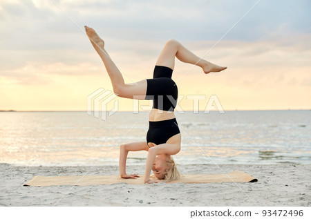 woman doing yoga headstand on beach 93472496
