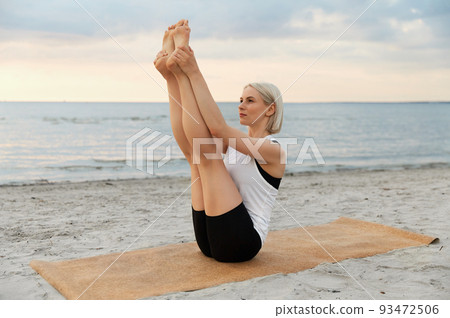 woman doing yoga boat pose on beach 93472506