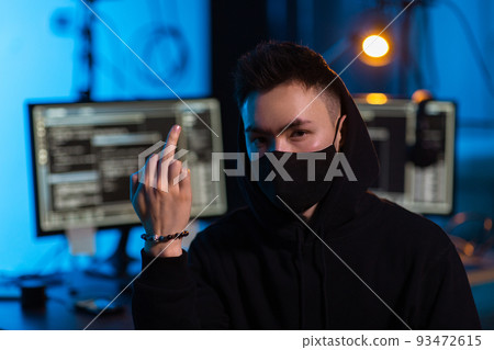 hacker in mask showing middle finger in dark room 93472615