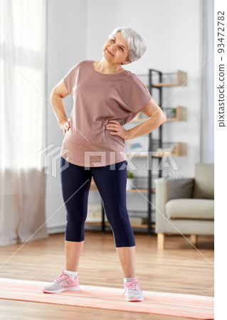 smiling senior woman exercising on mat at home 93472782
