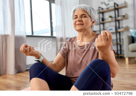 happy senior woman meditating on mat at home happy senior woman meditating on mat at home 93472796