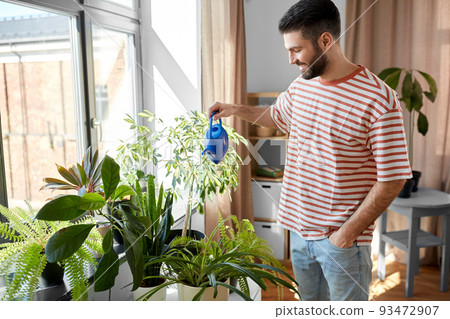 happy smiling man watering flowers at home happy smiling man watering flowers at home 93472907