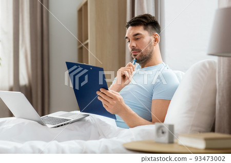 man with laptop working in bed at home bedroom 93473002