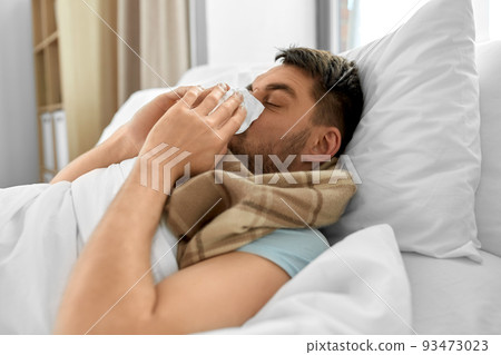 sick man blowing nose lying in bed at home sick man blowing nose lying in bed at home 93473023