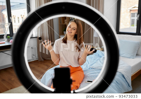 girl blogger with ring light applying make up 93473033