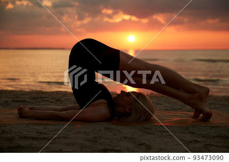 woman doing yoga plow pose on beach 93473090