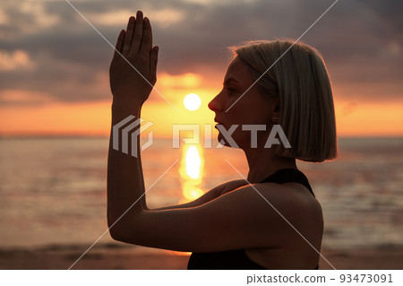 woman meditating on beach over sunset 93473091