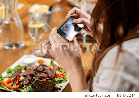 women with phone photographing food at restaurant women with phone photographing food at restaurant 93473214
