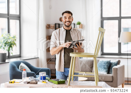 man with tablet pc renovating old chair at home man with tablet pc renovating old chair at home 93473224