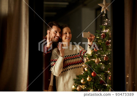 couple taking selfie at christmas tree at home couple taking selfie at christmas tree at home 93473389
