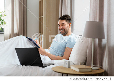 man with laptop working in bed at home bedroom 93473621