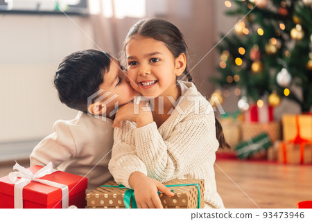 boy kissing sister with christmas gifts at home 93473946