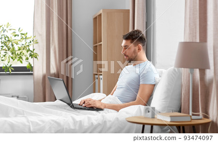 man with laptop in bed at home bedroom 93474097