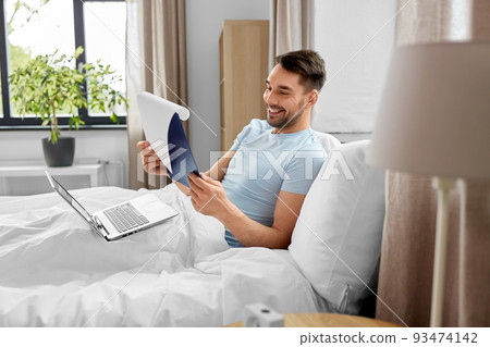 man with laptop working in bed at home bedroom 93474142