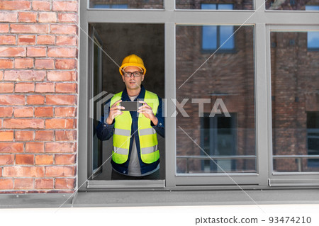 builder with smartphone taking picture at window builder with smartphone taking picture at window 93474210