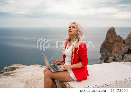 A woman is typing on a laptop keyboard on a terrace with a beautiful sea view. Freelancing, digital nomad, travel and vacation concept. 93478994