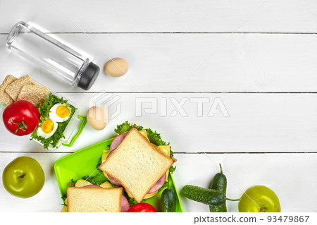 Healthy lunch box with sandwiches, eggs and fresh vegetables, bottle of water on rustic wooden background. Top view with copy space Healthy lunch box with sandwiches, eggs and fresh vegetables, bottle of water on rustic wooden background. Top view with copy space 93479867