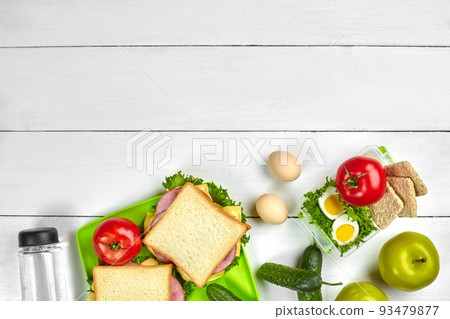 Healthy lunch box with sandwiches, eggs and fresh vegetables, bottle of water on rustic wooden background. Top view with copy space 93479877