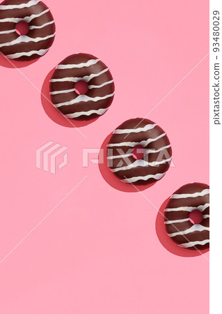 Food design with tasty chocolate glazed donut with white strips on coral pink pastel background top view pattern Food design with tasty chocolate glazed donut with white strips on coral pink pastel background top view pattern 93480029