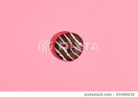 Food design. Close up high quality image of chocolate glazed donut with white strips on coral pink background Food design. Close up high quality image of chocolate glazed donut with white strips on coral pink background 93480036